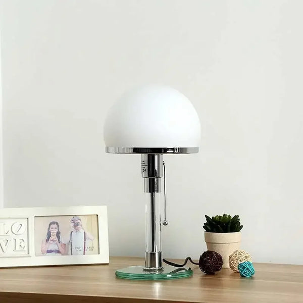 Bauhaus-style table lamp with opal glass shade and metal base on a wooden desk in a modern interior.