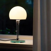 Elegant Bauhaus-style lamp with soft illumination, placed on a windowsill at night.