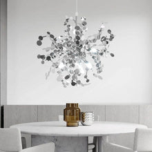 Contemporary silver pendant chandelier hanging over a round dining table, illuminating the modern dining space with cool white light.