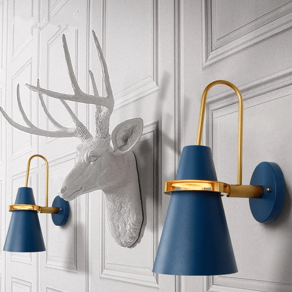 Industrial wall light in blue and gold finish, mounted on a white wall with decorative deer head sculpture.