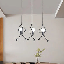 Modern Iron Little Man Ceiling Lamp – three black metal pendant lights with a unique human-shaped design, hanging over a dining table.