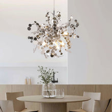 Modern silver chandelier hanging over a stylish dining space with minimalist furniture, casting a bright, elegant glow.