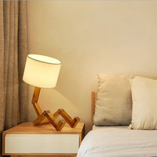 The WoodFlex Table Lamp placed on a nightstand beside a cozy bed, emitting warm light.